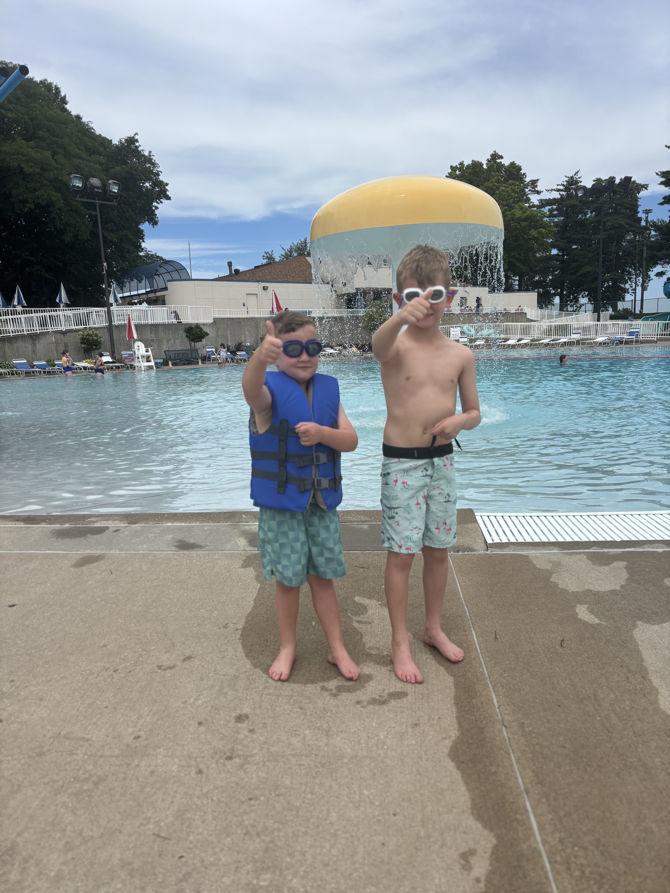 The boys poolside giving double thumbs up, goggles on