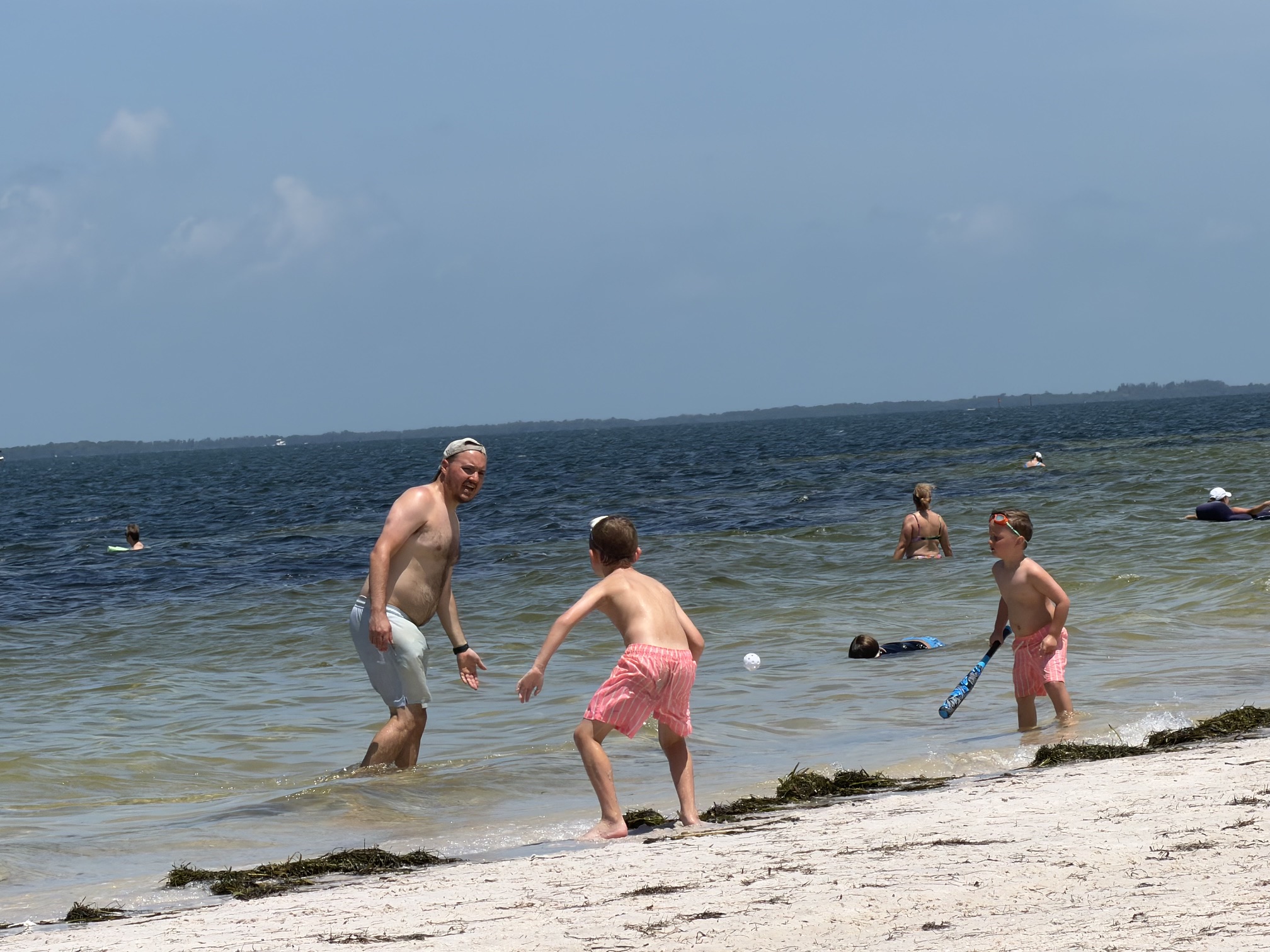 Beach wiffle ball in the shallows... dad pitching to two boys